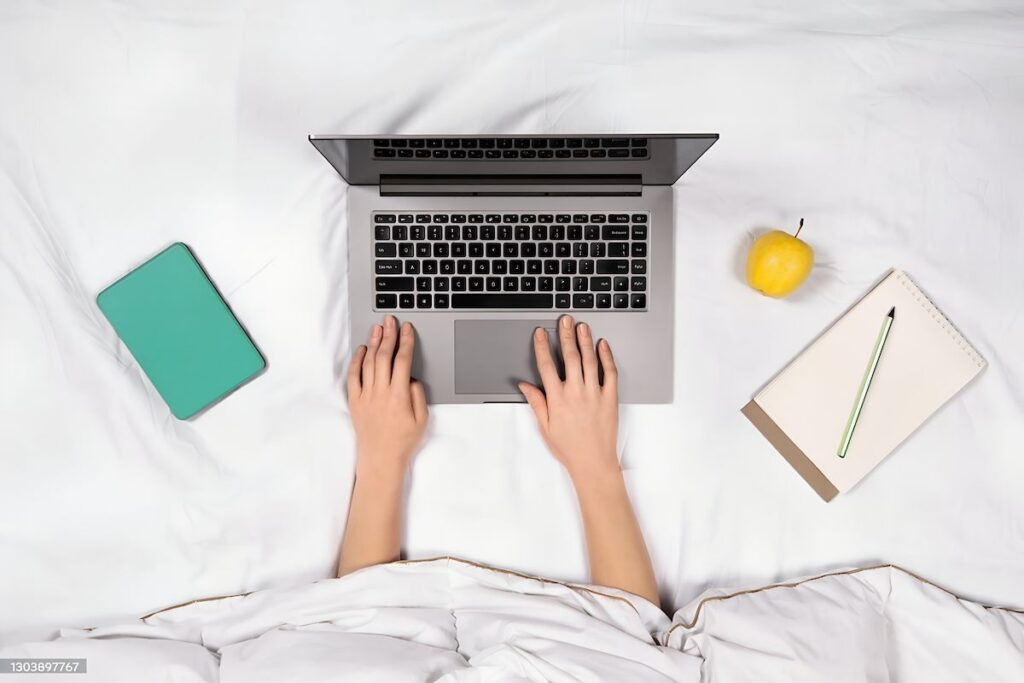 نمای بالا از فریلنسر مشغول کار با لپ‌تاپ در رختخواب؛ نماد از بین رفتن مرز فیزیکی بین استراحت و کار و حذف فضای گذار در زندگی شغلی.