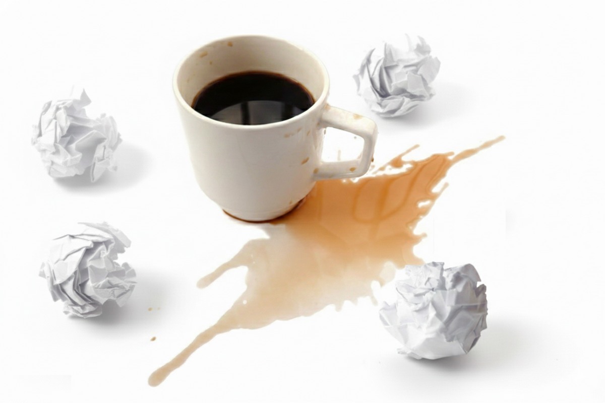 کاغذهای مچاله شده و فنجان قهوه، نمادی از فشار کاری بیش از حد و آشفتگی ذهنی به عنوان یکی از علل اصلی فرسودگی شغلی.